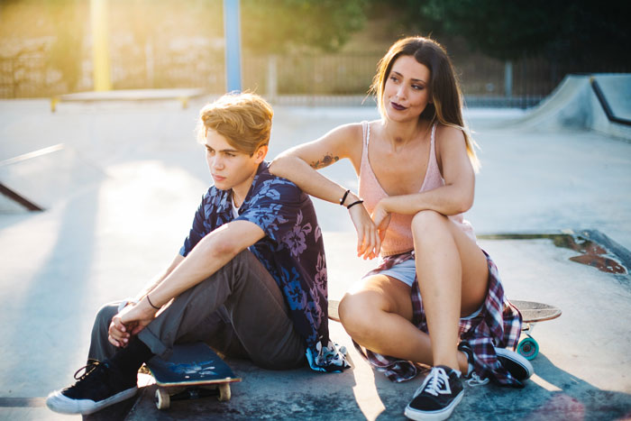 Teen siblings in Austria sitting at skatepark enjoying free time while parents are busy with babysitting duties nearby Teen siblings in Austria sitting at skatepark enjoying free time while parents are busy with babysitting duties nearby