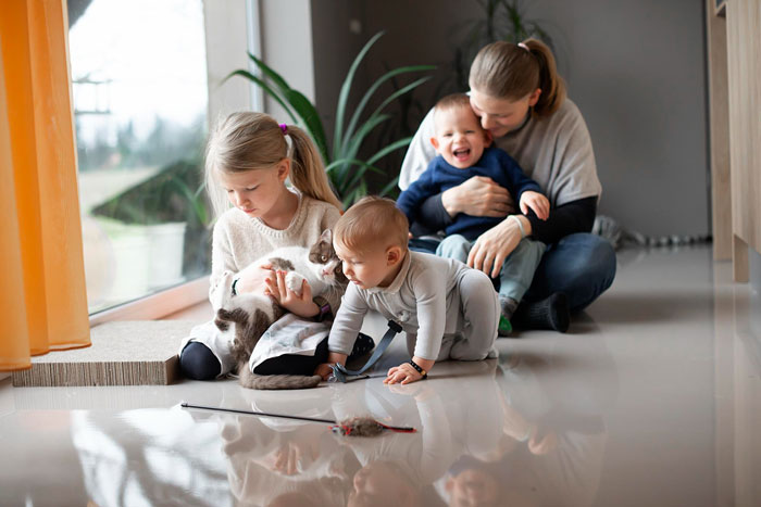 Mother and siblings babysitting toddlers at home in Austria, playing with a cat near a large window on the floor. Mother and siblings babysitting toddlers at home in Austria, playing with a cat near a large window on the floor.