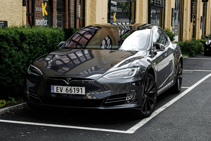Black Tesla electric car parked in an EV charging spot on a city street near commercial buildings.