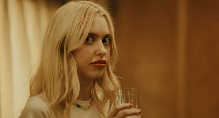 Young woman with blonde hair holding a glass, captured in a warm-toned background.