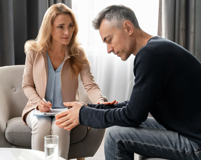 Woman offering support to a distressed man during a counseling session about partner's phone secrets.