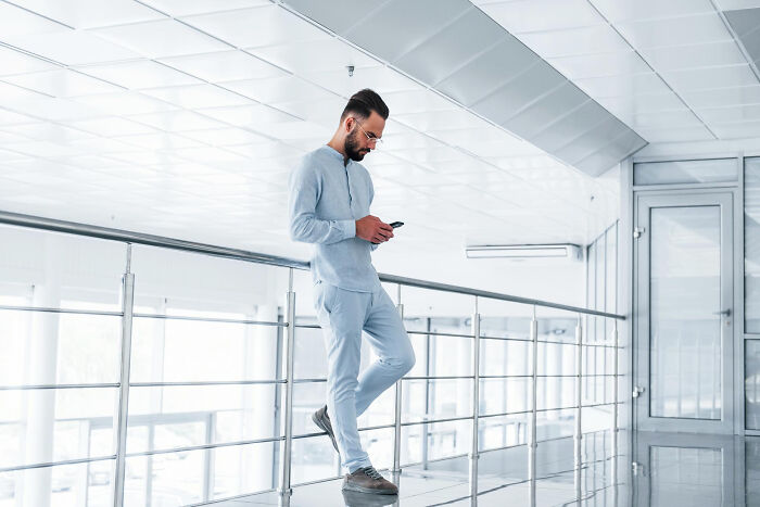 Man leaning on railing using phone in modern bright corridor.