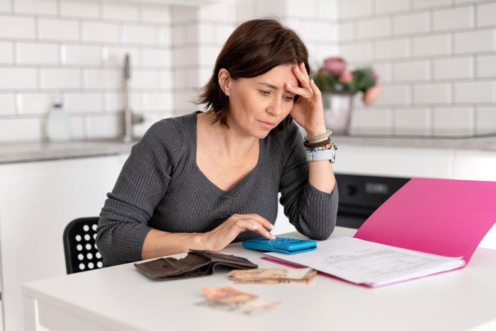 Woman calculating finances with a calculator and documents, stressed about paying off daughter student loans at home.