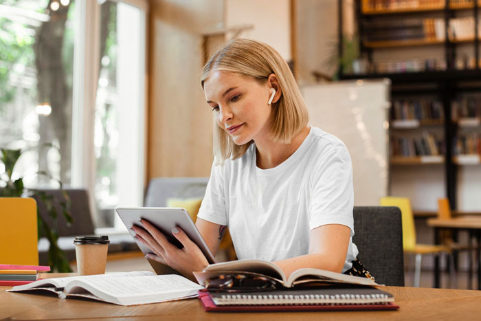 Young woman focused on tablet with books open, studying in a cozy space related to paying off daughter student loans.