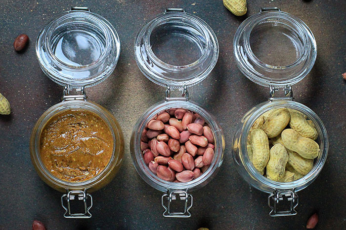 Three glass jars containing peanut butter, shelled peanuts, and unshelled peanuts on a dark surface, highlighting peanut allergy risk. Three glass jars containing peanut butter, shelled peanuts, and unshelled peanuts on a dark surface, highlighting peanut allergy risk.