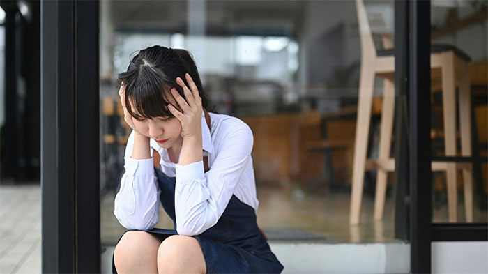 Young woman looking distressed sitting outside a glass door, reflecting on moments of finally getting even with a bully.