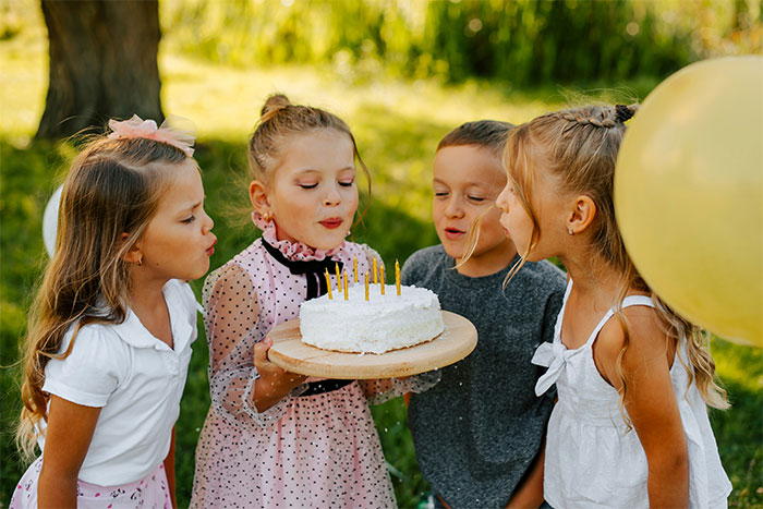Four children celebrating a birthday outdoors, blowing out candles on a cake, capturing a joyous moment of getting even with a bully.