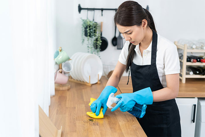 Young woman wearing blue gloves cleaning a wooden table, symbolizing the moment they finally got even with a bully.