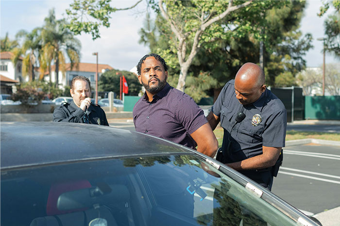 Man being handcuffed by police officers outside a car, illustrating the moment someone got even with a bully.