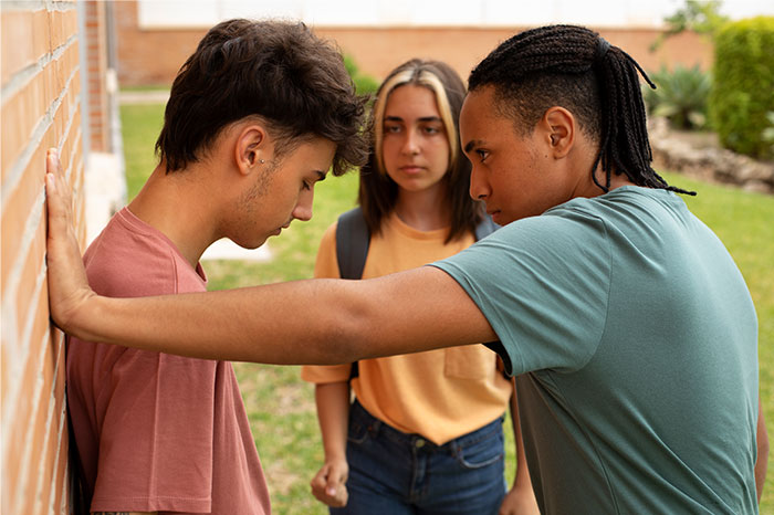 Teen standing against a wall with another teen confronting him, while a girl watches, illustrating bullying and revenge moments.