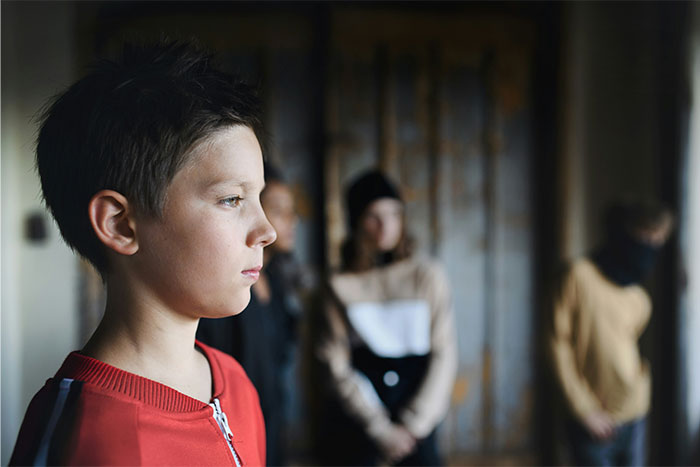 Young boy in a red jacket showing confidence while standing apart from a blurred group, reflecting a moment of getting even with a bully.