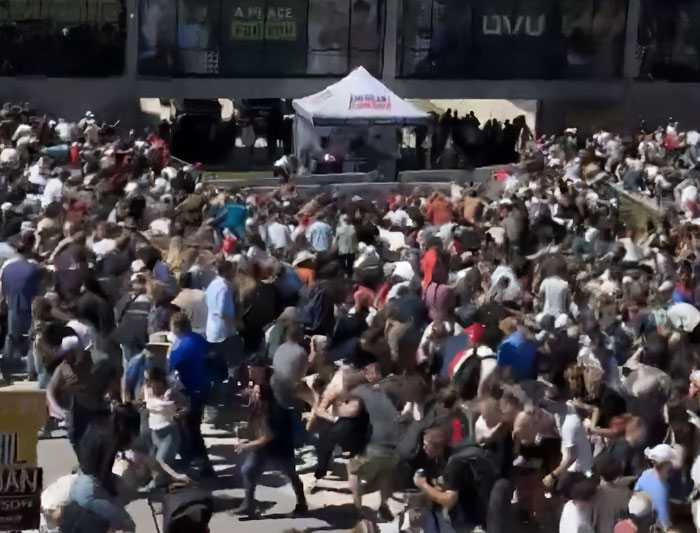Crowd scene with a mystery bearded man spotted cheering and looking back during Charlie Kirk's attack event outdoors.