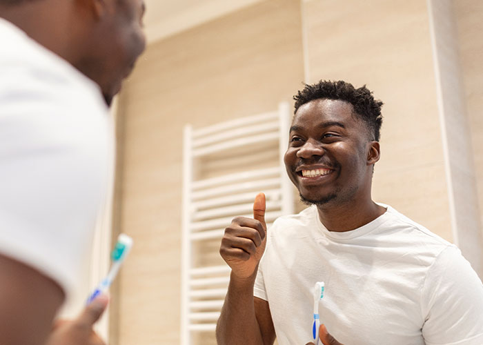 Smiling man holding a toothbrush and giving thumbs up in bathroom mirror reflecting life hacks that actually work.