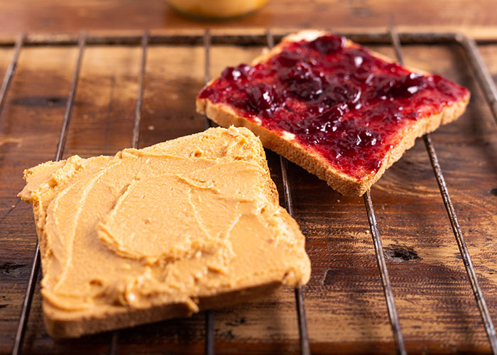 Two slices of bread on a wooden rack with peanut butter on one and jelly on the other, illustrating life hacks that work.
