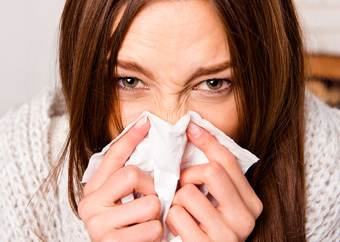 Young woman holding tissue to nose, demonstrating life hacks that actually work for cold and allergy relief.