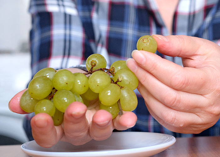 Person holding and picking green grapes from a bunch, illustrating life hacks that actually work for healthy snacking.