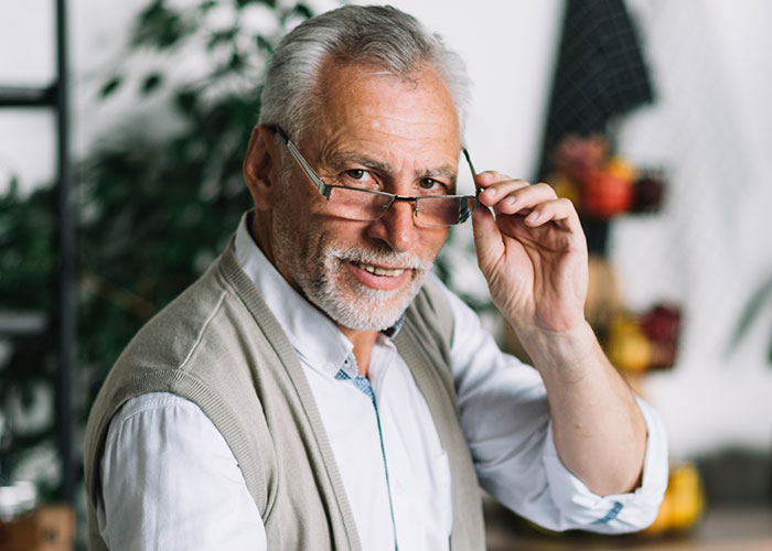 Older man with gray hair and glasses smiling and adjusting glasses, illustrating life hacks that actually work.