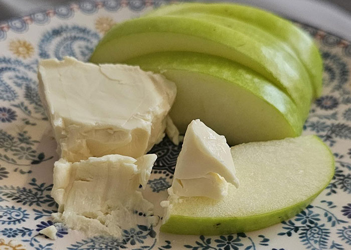Sliced green apple and cream cheese on a decorative plate, showcasing a simple life hack snack idea.