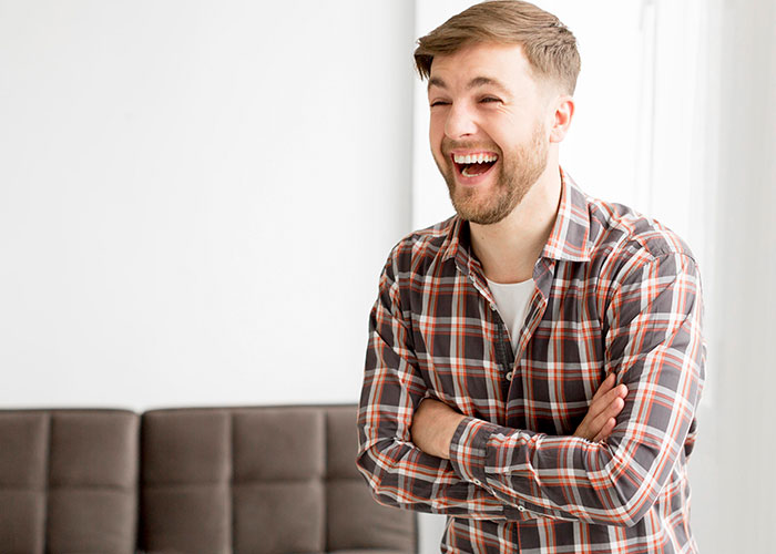 Young man laughing with arms crossed in bright room, illustrating life hacks that actually work for everyday solutions.