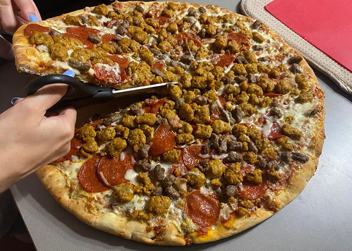 Person using scissors to cut a large meat-topped pizza illustrating creative life hacks that actually work in everyday tasks.