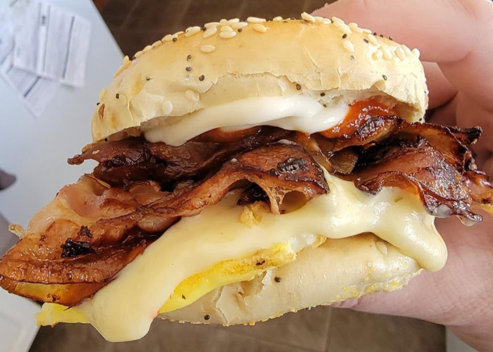 Close-up of a hand holding a bacon and cheese sandwich showing a practical life hack for easy breakfast preparation.
