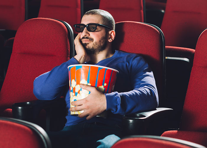 Man wearing 3D glasses sitting in a theater with popcorn, illustrating life hacks that actually work for better experiences