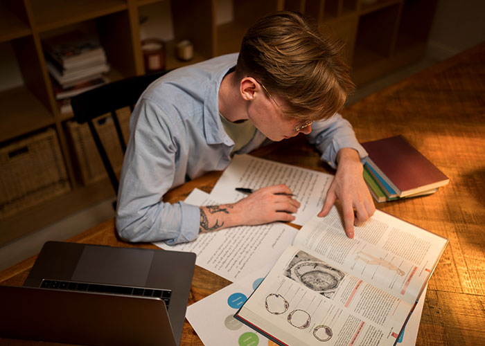 Person sitting at a wooden table, studying life hacks that actually work with books, papers, and a laptop nearby.