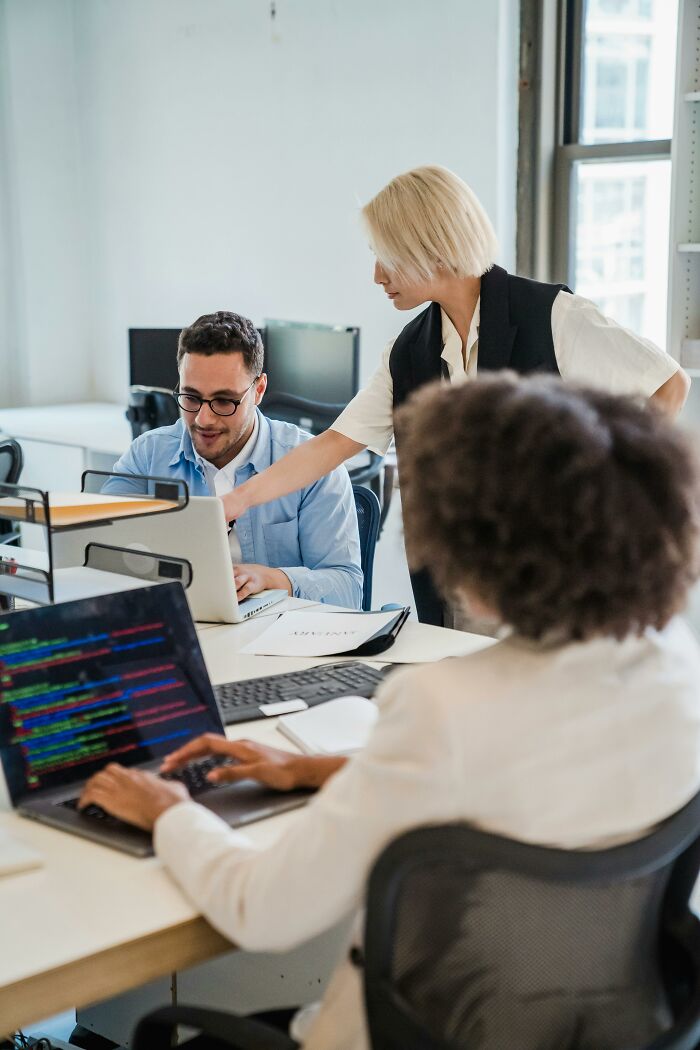 Office workers collaborating on laptops in a modern workspace, illustrating corporate hell challenges and unhinged tricks.