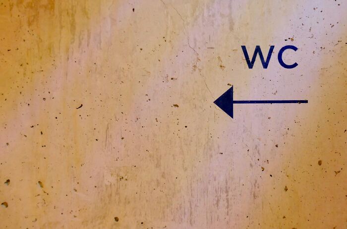 Worn wall with arrow and WC sign, symbolizing the struggles and escape routes of corporate hell.