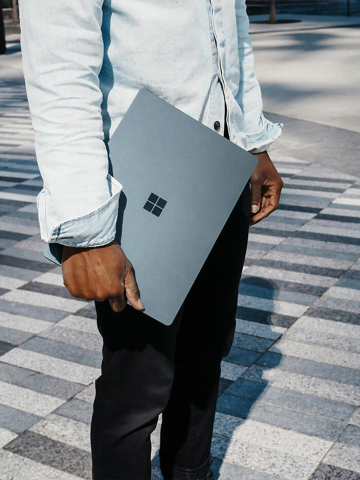 Man holding a Microsoft laptop outdoors, symbolizing corporate hell and unhinged tricks for workplace survival.