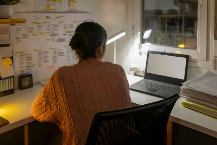 Person working late in a dimly lit office surrounded by paperwork and a laptop reflecting corporate hell challenges.