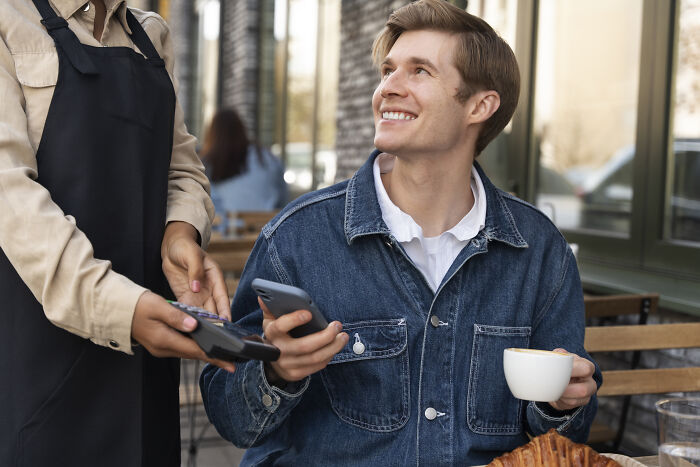 Man on a date smiling while paying with phone, illustrating common tests women use for dating red flags.