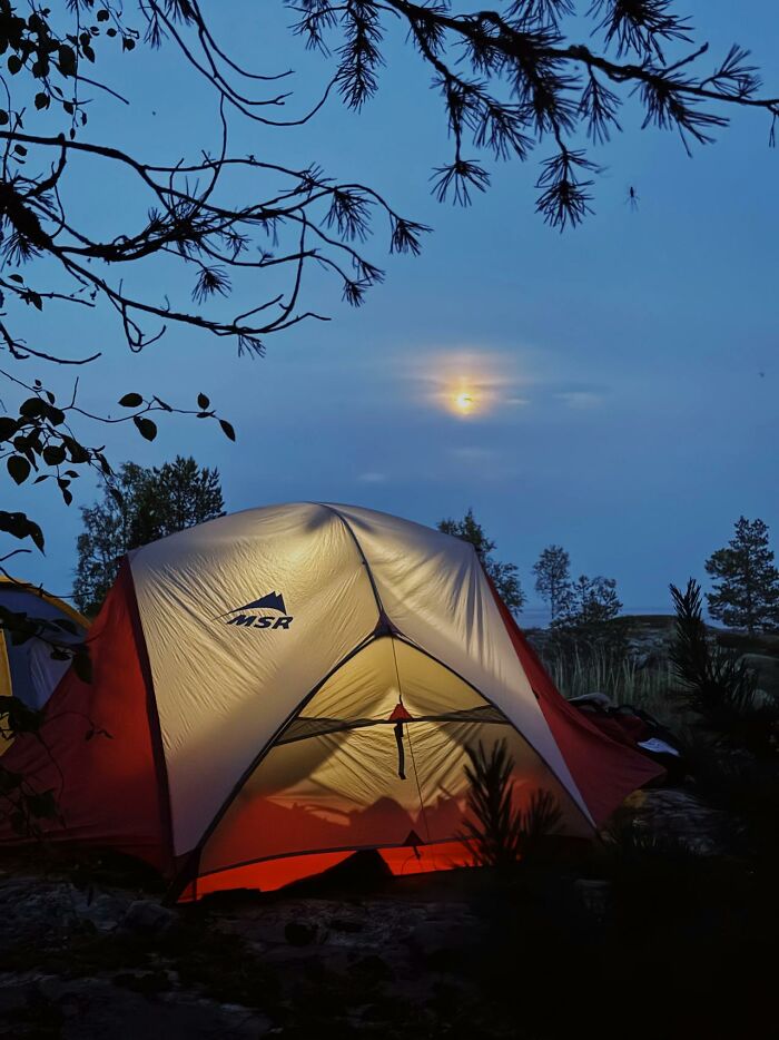 Tent glowing at dusk surrounded by trees, evoking the creepy things encountered while alone in the woods.