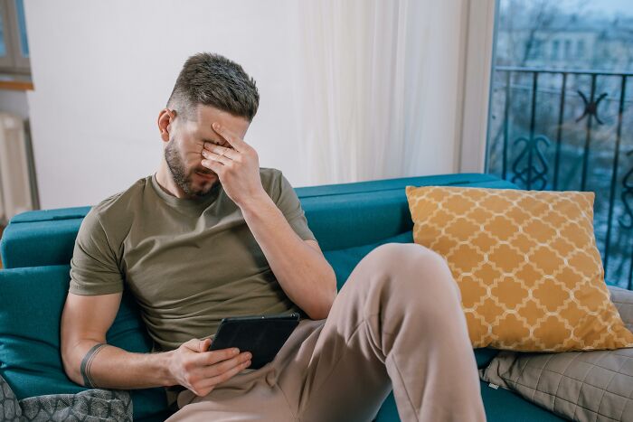 Man stressed on couch, holding tablet, reflecting on pressure and sad ending in marriage life updates.