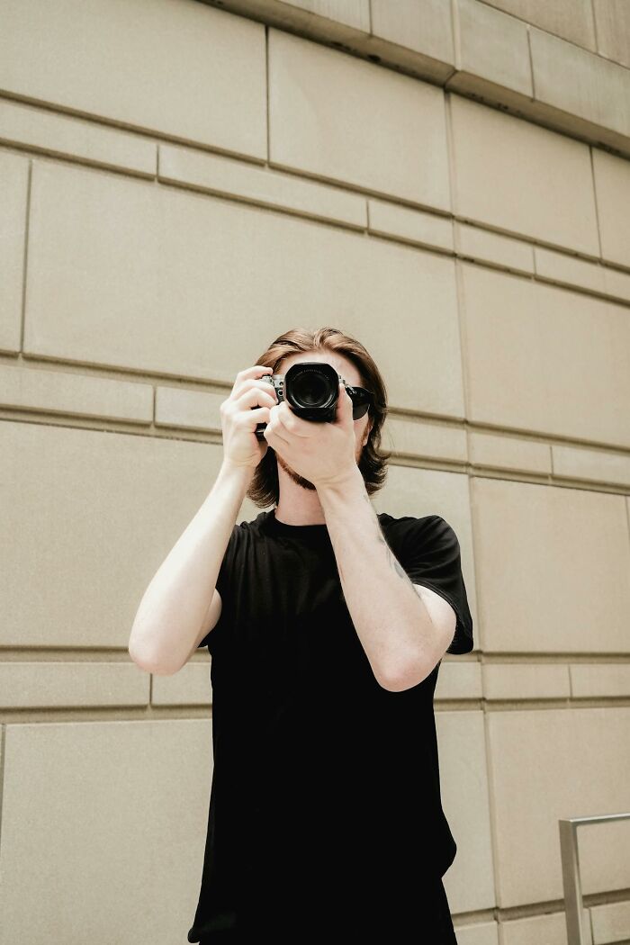 Young man holding a camera taking a photo against a beige wall, illustrating people who were the villain in someone else's story.