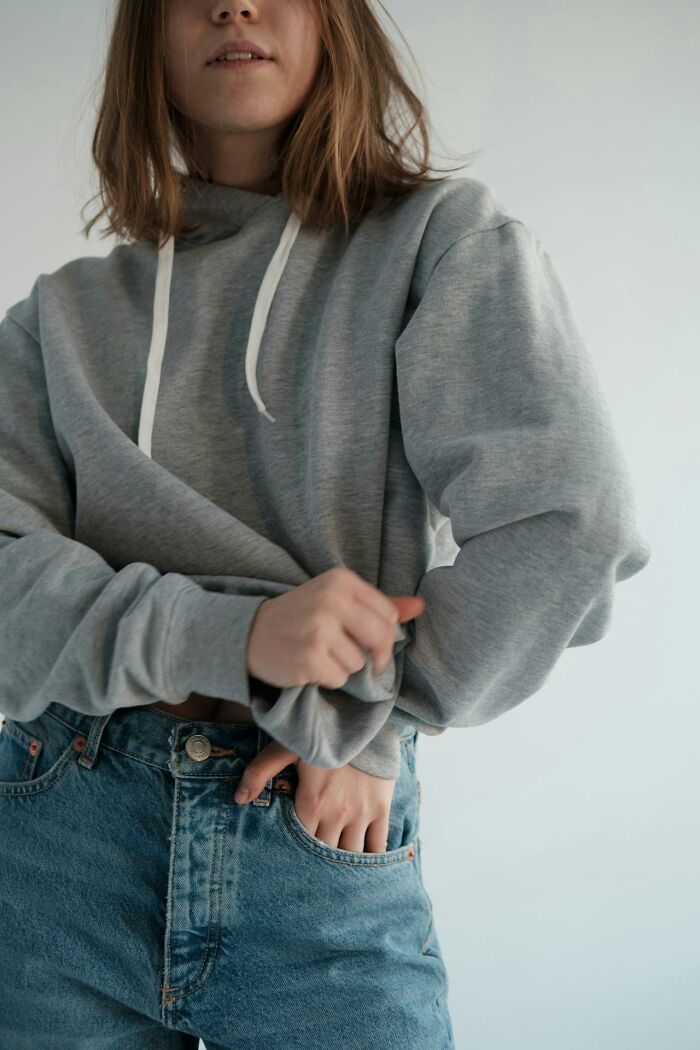 Young woman in a gray hoodie and jeans adjusting her sleeve, illustrating things women are not allowed to do that men can do freely.