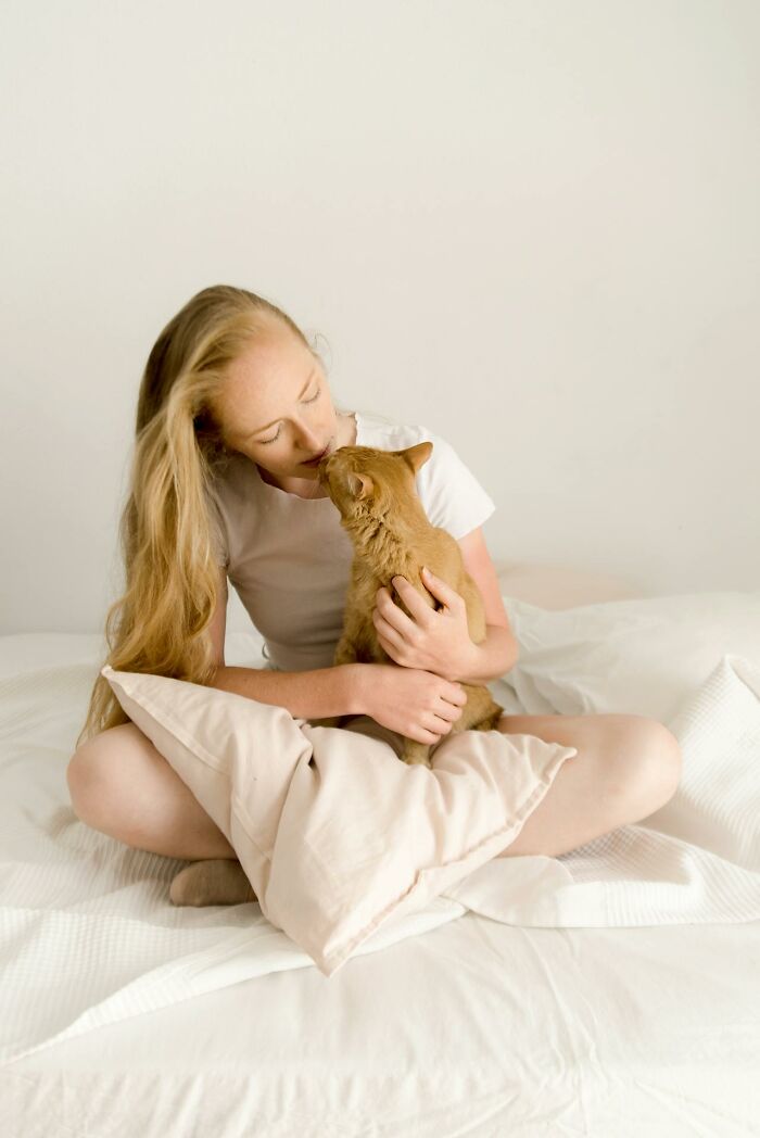Young woman sitting on bed with pillow holding and cuddling an orange cat showing unbelievable moments of true connection.