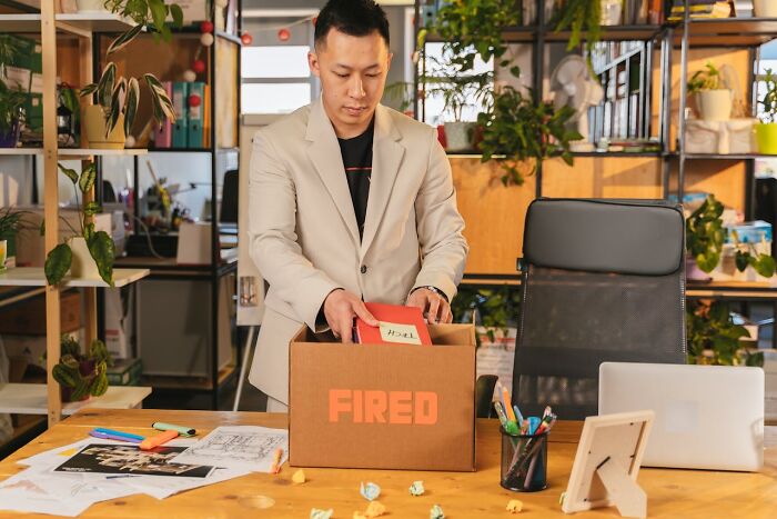 Man packing personal items in a box labeled fired, representing people who were the villain in someone else’s story.
