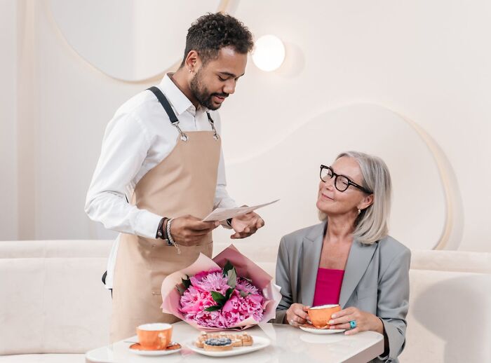 Man in apron handing a card to a woman with flowers on the table capturing unbelievable moments that were actually true