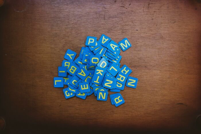 Blue letter tiles scattered on a wooden surface representing single letters for a 26-question quiz challenge.