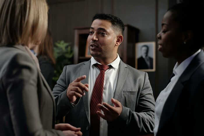Man in gray suit and red tie discussing professions that people believe are not relationship material with two women.