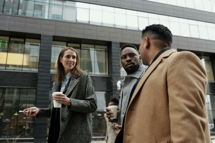 Three professionals having a conversation outside an office building, illustrating advanced stupid out-of-touch remarks.