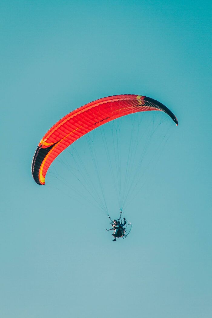 A person paragliding with a red and orange wing against a clear blue sky symbolizing survival moments.