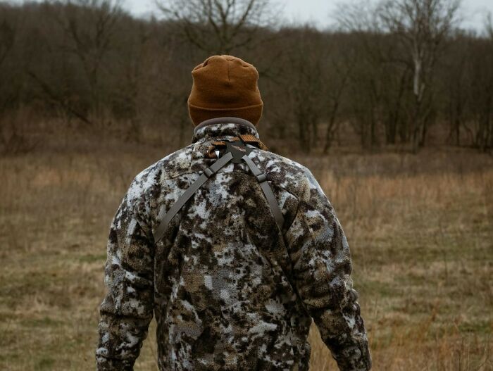 Person in camouflage jacket and brown hat standing outdoors in a field, illustrating unholy health violations in restaurants.