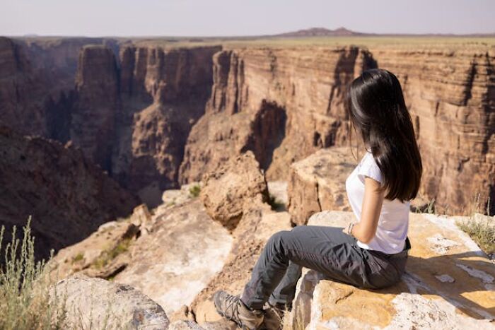 Woman sitting on rocky cliff edge, overlooking vast canyon landscape, evoking mystery of real-life hexes and spells.