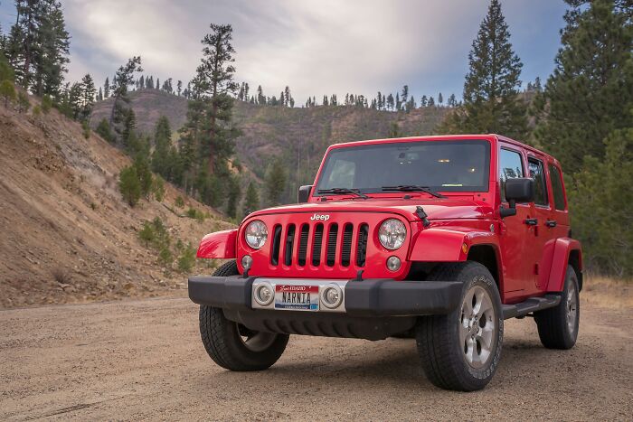 Red Jeep parked on a dirt road with forested hills, illustrating netizens exposing companies that sabotage their own products.