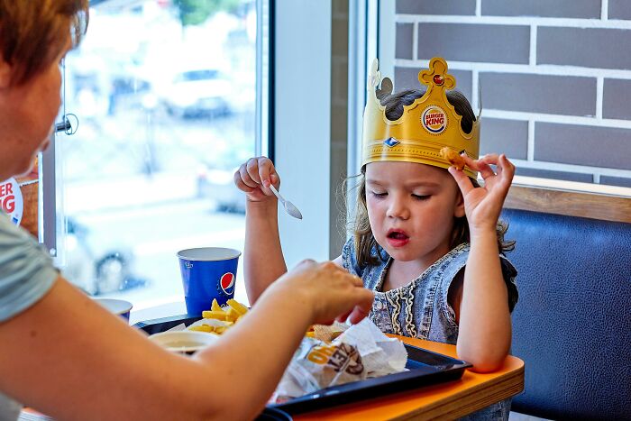 Young child wearing a Burger King crown eating fries with an adult, illustrating real-life stories of people becoming what they once hated.