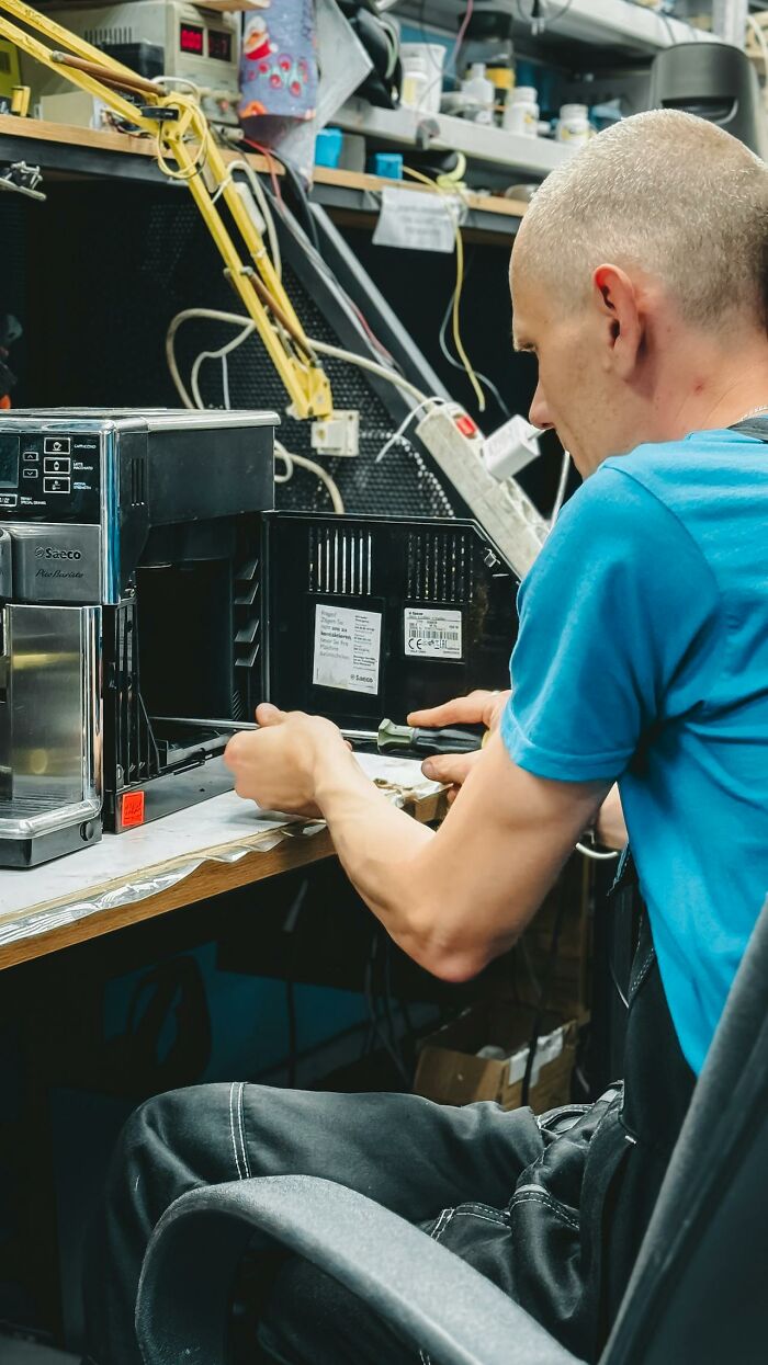 Technician repairing a high-end coffee machine in a workshop among tools and electronic equipment for ultra-wealthy people.