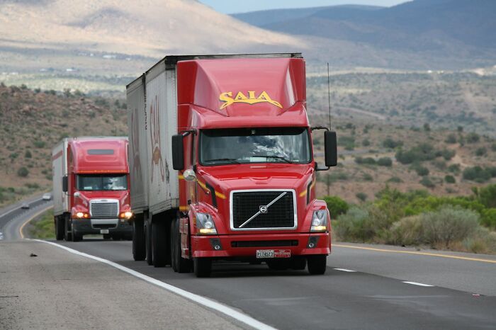 Red semi-trucks driving on a highway through a mountainous desert landscape, highlighting survival moments on the road.