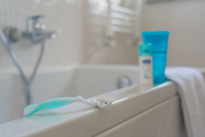 A broken disposable razor resting on a bathtub edge with bathroom items blurred in the background, showing product sabotage.